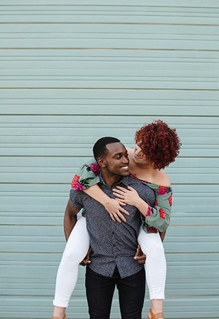 Two people embracing and laughing against a pale painted wall