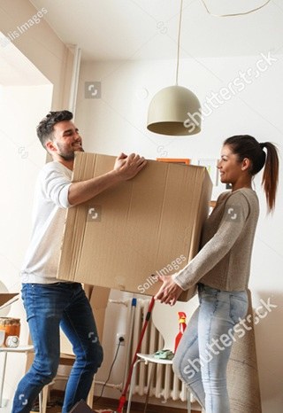 Two people carrying a large box together through a bright room