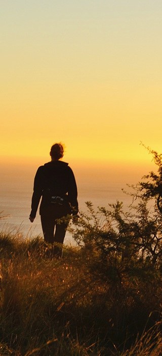 A person walking a coastal path toward the setting sun