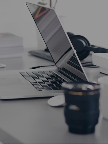 A laptop, headphones and camera lens arranged on a bright desk