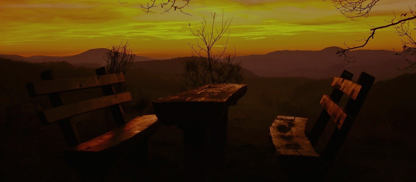Empty wooden benches on a hillside looking out over a valley at sunset